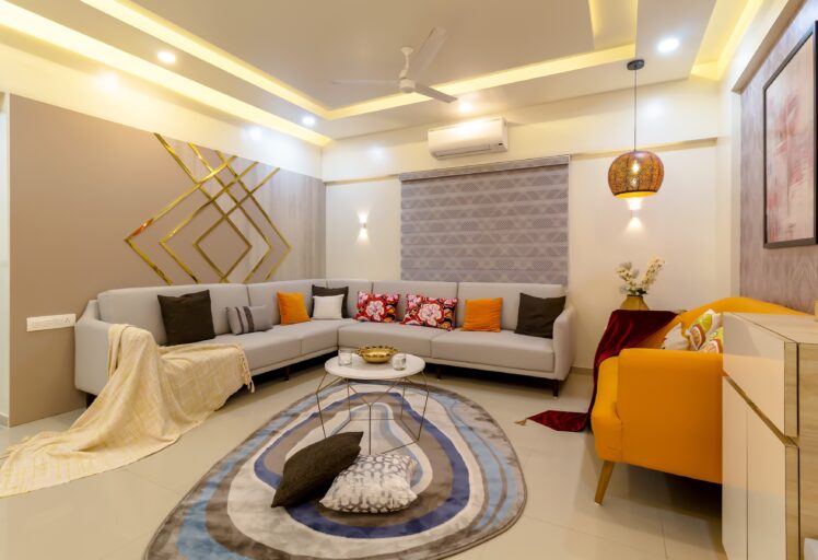Modern living room with L-shaped sofa, colorful cushions, ceiling lights, and patterned rug.